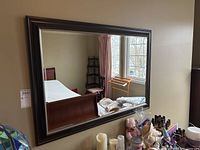 Full view of large rectangular wall mirror with dark brown frame, hanging on the wall reflecting room interior.