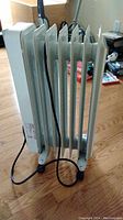 Side view of white oil-filled radiator heater with power cord on hardwood floor.