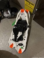 Full snowshoe showing white plastic frame with black bindings and orange tips.