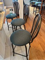 Three metal kitchen stools lined up showing greenish-blue fabric seats and metal frame with backrests.