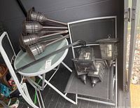 Lot contents showing round glass-top patio table, two folding chairs with black mesh fabric, and six solar garden lights of two different styles.