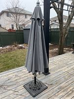 Gray patio umbrella closed and attached to metal stand on wooden deck.