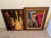 Two framed paintings displayed side by side, one featuring a child looking at candles, the other an elderly man reading.
