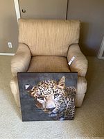 Beige upholstered armchair with removable cushions and square leopard painting placed in front