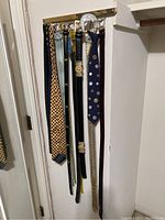 Photo of belts and ties hanging on a rack mounted on a wall.