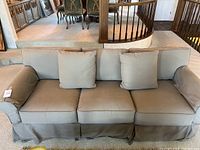 Front view of beige upholstered couch with three cushions and slipcover.