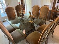 Full view of rectangular glass-top dining table with eight brown upholstered chairs arranged around it and two horse statues on the tabletop.