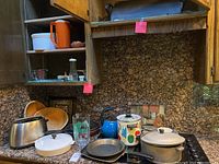 Wide view of kitchen cabinets with cookware and dishes inside and on countertop.