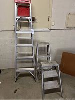Front view photo showing one large Werner aluminum step ladder and two smaller aluminum step stools.