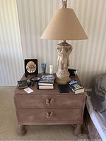 Wide view of nightstand holding elephant base lamp, books, remotes, and other items