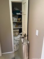 Closet view with shelves holding folded linens including tablecloths, towels and bedding with curtain panels on bottom shelf