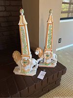 Pair of ceramic lion obelisks placed on a brick hearth, showing full view of both items