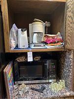 Microwave oven inside cabinet with coffee maker on upper shelf, towels, coffee grinder, candle holders and artwork visible