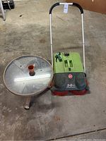 Full view of the round glass top side table and Hoover outdoor sweeper placed on floor.