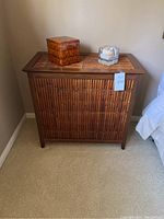 Closed bamboo hamper with rectangular shape, lattice front design, warm brown wood color, two decorative items on top.