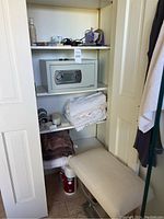 View of the closet showing shelves with a small electronic safe, towels, fabric, and various personal items.
