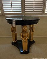 Full view of semicircular black side table with three gold figurines as supports on black triangular base.