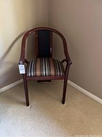 Front view of wooden accent chair with striped upholstered seat and curved backrest on beige carpet in a corner.