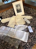 Vintage baby clothing items along with embroidered linens and framed military portrait photograph arranged on granite surface.