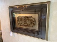 Framed wall art hung on wall, showing the multilayered frame and grape vine relief centerpiece under glass.