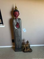 Photo showing the full height of the tall wood-carved Zen statue alongside the smaller seated Buddha statue on the floor.