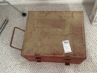 Top view of closed red metal toolbox covered in dust and dirt.