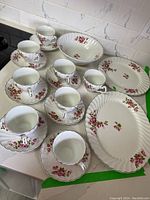 Photo showing full set of 5 cups, 5 saucers, and 2 serving plates with floral rose pattern and gold rims on white ironstone.