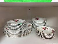 Three stacks of Johnson Bros Snowhite Regency ironstone china dishes on a shelf, showing the floral rose pattern and scalloped edges.