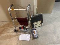Overall view of the aluminum walker, small healthcare accessories, white board, wheelchair cushions, and cane tips arranged on floor.
