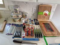 Overview of kitchen items including cutting boards, knives, skewers, storage containers, and small utensils all new in packaging.