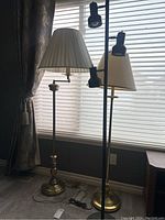 Brass table lamp and black floor lamp with three adjustable spotlights shown together in front of window with blinds.