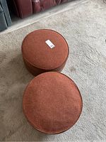 Two red round ottomans on light-colored carpet, one with casters and one without.
