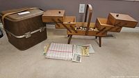 Photo of the closed wooden expandable sewing box with buttons inside, brown carrying case for serger and some papers/manuals