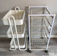 Two storage trolleys side by side; white trolley with three mesh drawers on left and white frame trolley with wire baskets on right.