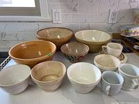 Assorted vintage mixing and pudding bowls on countertop alongside vintage cups and saucers, showing various sizes and signs of wear including crazing and chips.