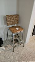 Vintage metal framed chair with brown vinyl upholstery and attached fold-down metal step stool. Condition issues visible.