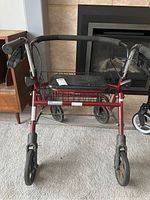 Front view of the red metal walker with black handles, brakes, seat, and wheels.