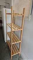 Full view of the wooden four-tier shelf in a garage setting next to a white cabinet and refrigerator.