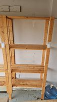 Front view of wood shelf unit showing four slatted shelves and vertical beams with drill holes.