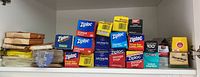 Shelf with 11 boxes of Ziploc storage bags and other food storage bags in various sizes, colors blue and yellow mainly, including sandwich bags and larger storage bags.