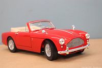 Front and side view showing red paint, chrome grille and bumper, wire-spoke wheels, beige interior, and convertible top folded down