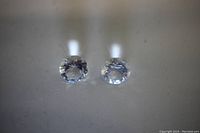 Close up image showing two clear round cut topaz loose gems placed side by side on a reflective surface, highlighting their transparency and facets.