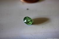 Oval cut green garnet loose gem placed on a surface, showing color and shape.