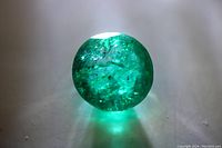 Close-up photo of the round cut green emerald gemstone showing rich green color and internal inclusions.