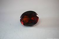 Clear close-up of the oval cut rhodolite red garnet loose gem on a plain background showing facets and transparency.