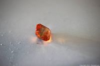 Close-up photo of the orange Asscher cut sapphire gemstone showing facets and color from an angle.