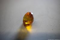 Side angled close-up photo showing the depth and orange color of the loose round cut sapphire gemstone.