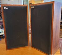 Front view of both Ohm Model E speakers with black cloth covers and wood cabinets.