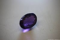 Close up side angle of oval faceted purple amethyst gem showing facets and depth of color.