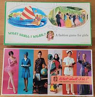 Two vintage board game boxes: 'What Shall I Wear?' with a sailing and ball scene illustration and 'What Shall I Be?' featuring women in varied career uniforms and outfits on the cover.